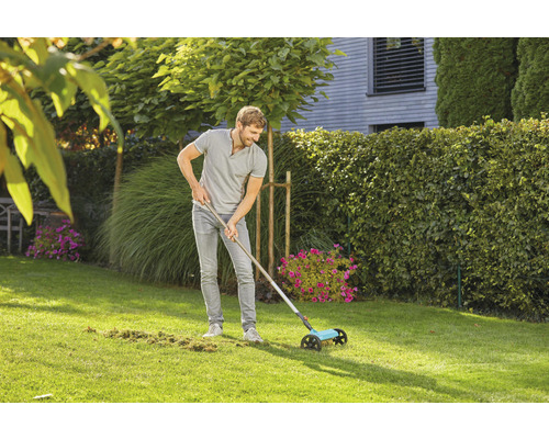 Een man gebruikt een gazonveger in de tuin om gazonafval te verwijderen.