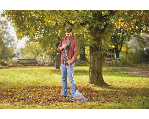 Man met bladhark in de tuin, herfstbladeren op het gazon.