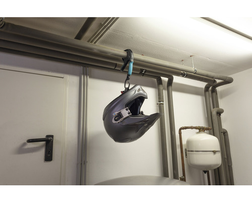 Een motorcrosshelm hangt met een buisklem aan een verwarmingsbuis.