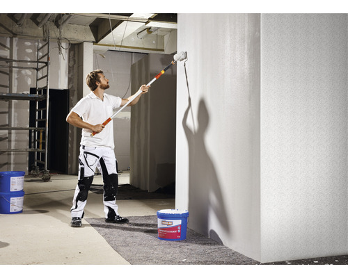 Een man schildert een muur met een verfroller in een ruwbouw.