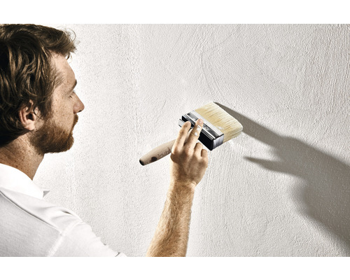 Een man schildert een muur met een platte kwast.