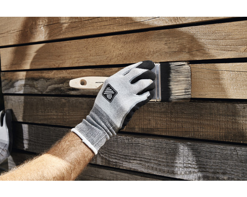 Een persoon draagt handschoenen en verft hout met een kwast.