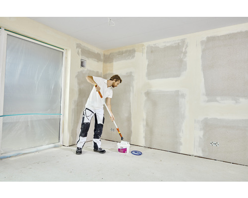 Man renoveert kamer met verfroller en verfemmer. Muren zijn voorbereid om te schilderen.