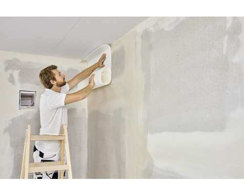 Man behangt een muur met een rol behang op een ladder