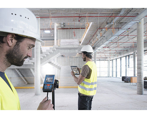 Twee bouwvakkers gebruiken een digitale laser afstandsmeter en een tablet op een bouwplaats.
