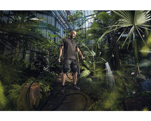 Een man bewaterd planten in een kas met een tuindouche.