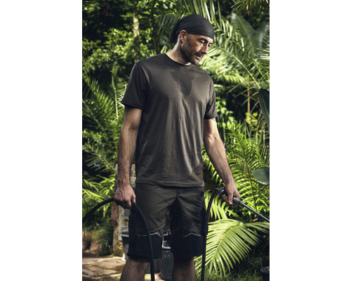 Een man in werkkleding houdt een tuinslang vast in een tuin.