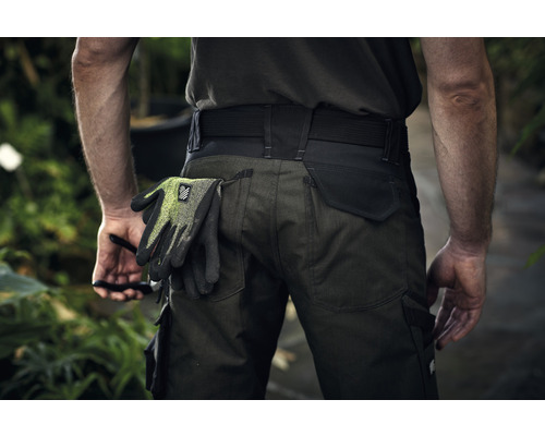 Een persoon draagt een werkbroek met werkhandschoenen in de achterzak.