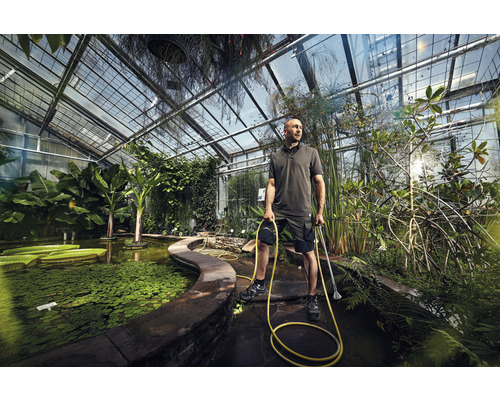 Man met waterslang en vijverslibzuiger in een kas met vijver