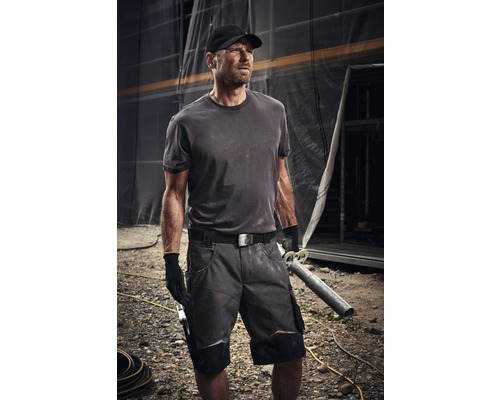 Vakman draagt werkkleding met korte broek, T-shirt, riem en handschoenen op een bouwplaats