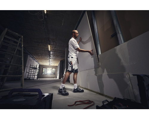 Een man monteert een gipsplaat op een metalen constructie in een kamer.