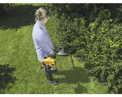 Vrouw werkt met een gele grastrimmer in de tuin.