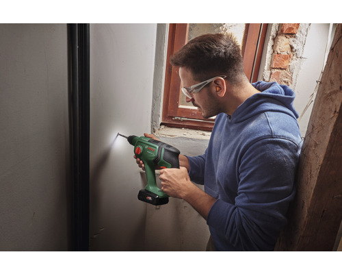 Een man boort met een accuboormachine een gat in een muur.
