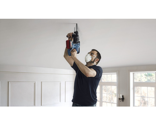 Een man boort met een boormachine een gat in het plafond.