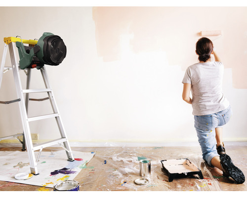 Scène van een vrouw die een muur schildert met een verfroller, inclusief ladder en ventilator