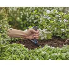 Een persoon gebruikt een montagegereedschap om een druppelaar in een tuinbewateringssysteem te installeren.