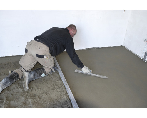 Ambachtsman bewerkt dekvloer in een kamer met een spaan.