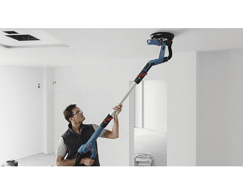 Een man schuurt een plafond met een langnekschuurmachine in een kamer.