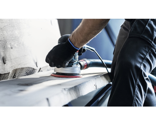 Een persoon schuurt hout met een elektrische excentrische schuurmachine.