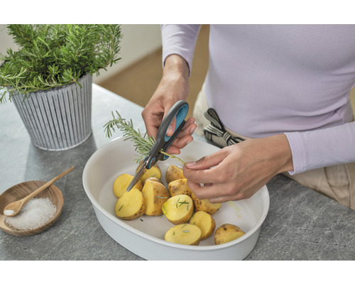 Persoon snijdt rozemarijn met een schaar boven een kom met aardappelen.