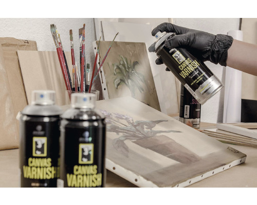 Spuitbus canvasvernis wordt aangebracht op een schilderij, omgeven door schildersezel en penselen.