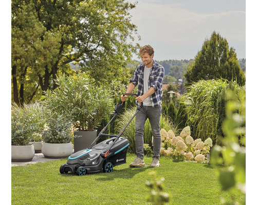 Een man maait het gazon met een Gardena gazonmaaier in de tuin.