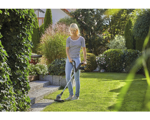 Vrouw gebruikt een grastrimmer in de tuin voor gazononderhoud.