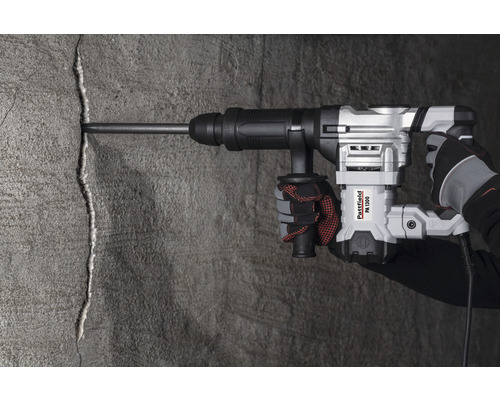 Een hand bedient een Pattfield PA 1300 breekhamer op een betonnen muur.