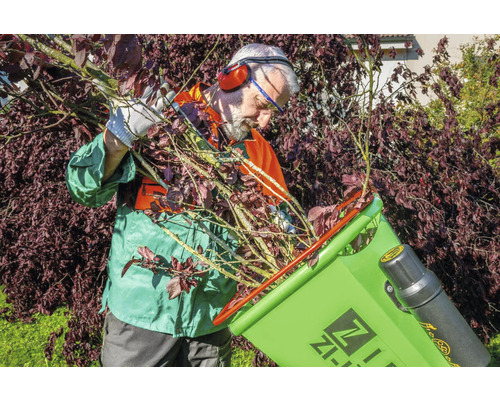 Een persoon vult een hakselaar met takken en twijgen in de tuin.
