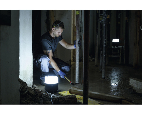 Ambachtsman aan het werk met bouwsteunen en een bouwlamp in een donkere ruimte.