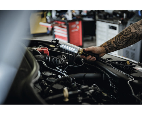 Een monteur inspecteert een automotor met een LED-werklamp.