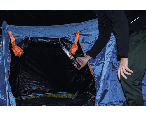 Persoon houdt een werklamp voor een tent.
