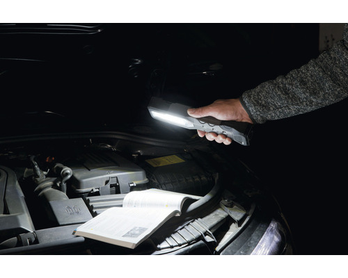 Een persoon houdt een LED-werklamp boven de open motorkap van een auto.