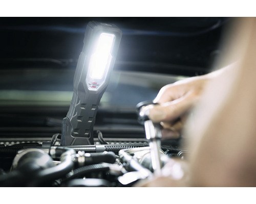 Werknemer met werkplaatslamp tijdens reparatie aan de automotor