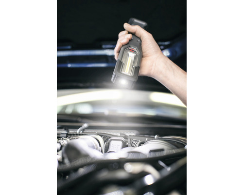 Hand houdt een accuhandlamp boven een automotor voor verlichting.