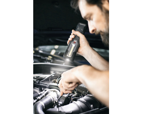 Een man verlicht een motorruimte met een werklamp.