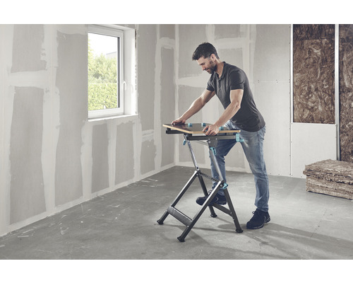 Man werkt met een werkbank in een ruimte met gipsplaten wanden en een raam.