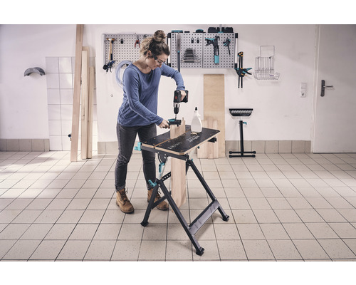 Vrouw werkt met een boormachine op een werkbank in een werkplaats.