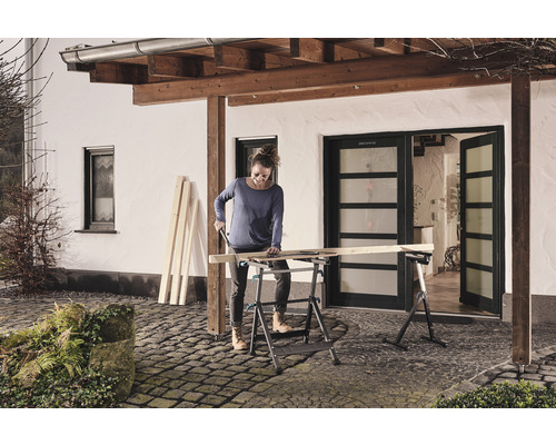 Vrouw zaagt hout op een inklapbare werkbank buitenshuis.