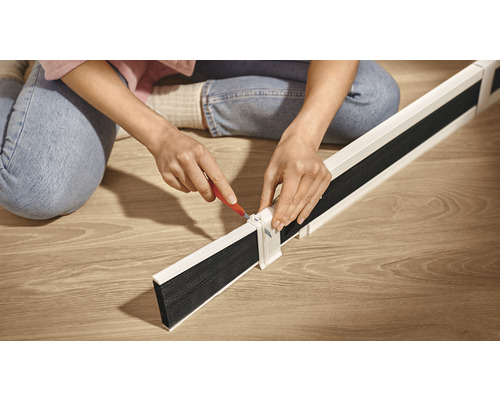 Een persoon monteert een tochtstrip op een houten vloer.