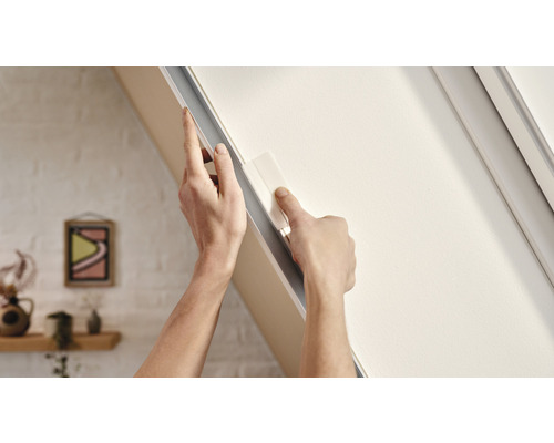 Iemand bevestigt een dakraamverduisteringsgordijn aan een raamkozijn.