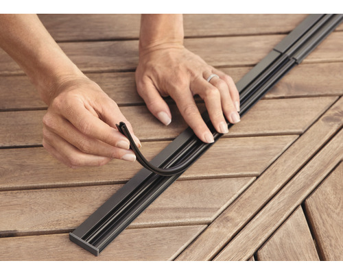 Persoon plaatst afdichtingsprofiel in een metalen rail op een houten tafel