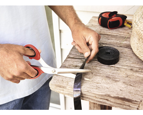 Iemand knipt een zwarte plastic band door met een schaar op een houten tafel.