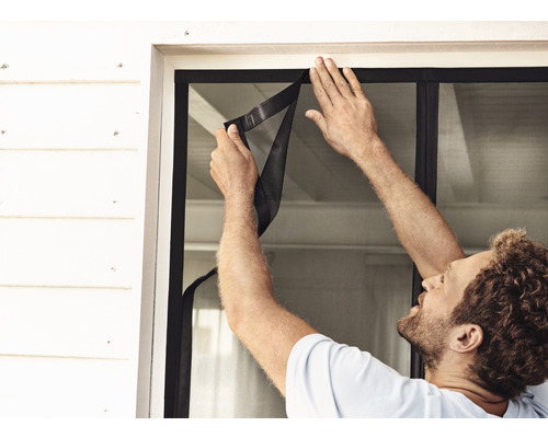 Man installeert een vliegengaas op het raam