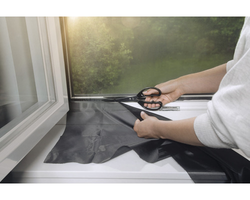 Met een schaar een verduisteringsfolie op maat knippen voor een raam.
