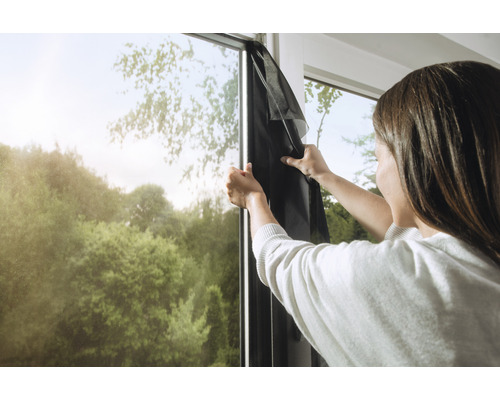 Vrouw bevestigt een zwart vliegengaas aan een raamkozijn.