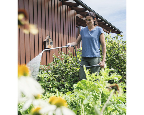 Een vrouw besproeit planten in de tuin met een gietstok