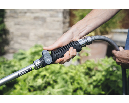 Een persoon houdt een tuinspuit van het merk Geka aan een tuinslang vast.