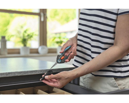 Persoon houdt een Gardena plantenschaar met beschermkap boven een lade.