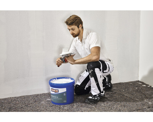 Man brengt mortel aan op een muur met een spaan. Op de voorgrond staat een emmer mortel.